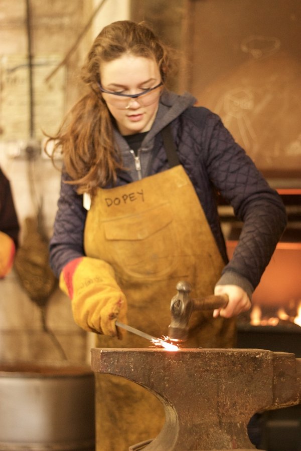 Ein Mädchen haut mit einem Hammer auf ein glühendes Stück Metall.