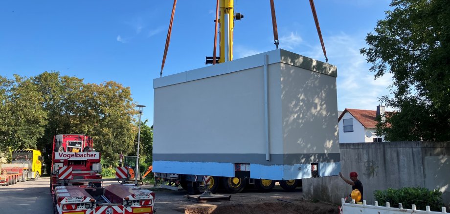 Ein großer grauer Container wird mit einem riesigen Kran in einer Grube abgesetzt.