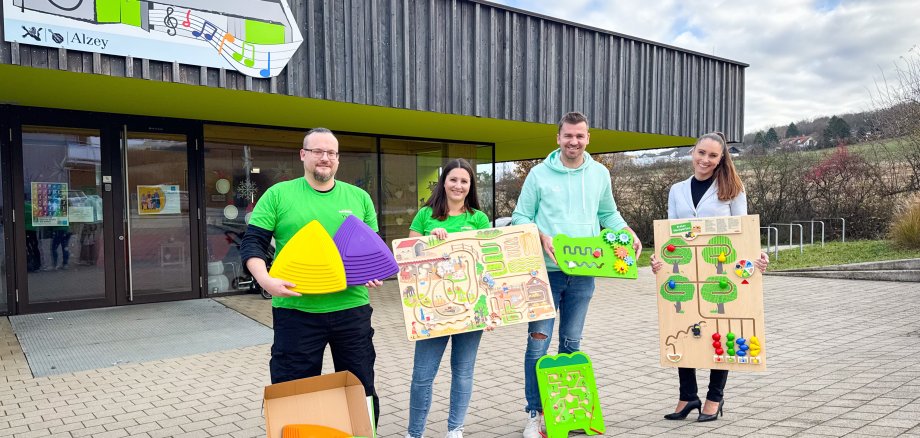 Yves Zentner, Kristina Hofrath, Kita-Leiter Pascal Weber und Sabine Schreiber vom Rheinhessen Center mit den neuen Motorik-Teilen vor dem Eingang der Kita "Haus der Klänge".