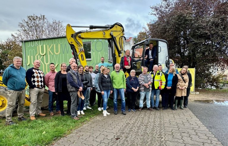 Viele Leute stehen um zwei Bagger herum, die vor einem grünen Gebäude stehen.