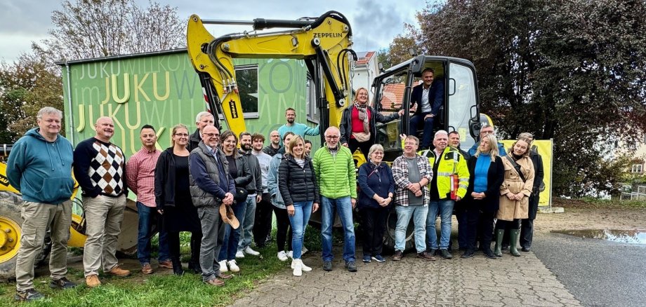 Viele Leute stehen um zwei Bagger herum, die vor einem grünen Gebäude stehen.