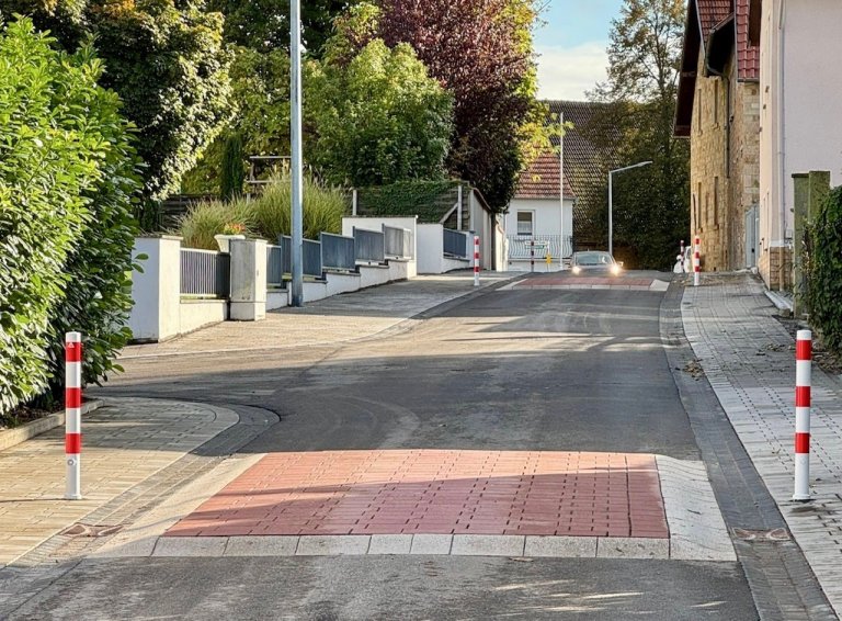 Zwei rote Erhebungen im Verlauf einer Straße. Im Hintergrund fährt ein Auto auf den Hubbel zu.